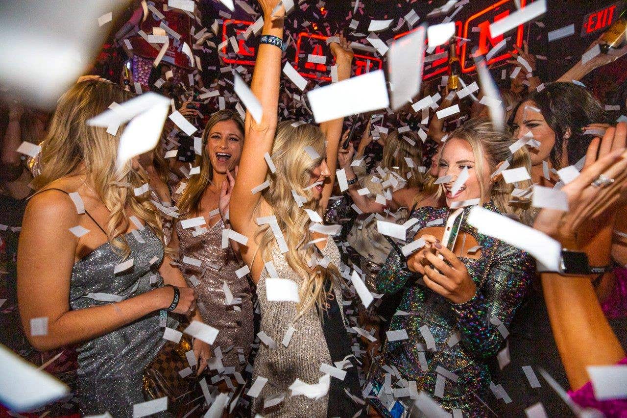 A group of women celebrating and dancing at a party with confetti falling around them.