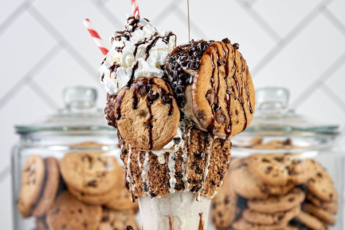 A decadent milkshake topped with whipped cream, chocolate chip cookies, and drizzled with chocolate syrup.