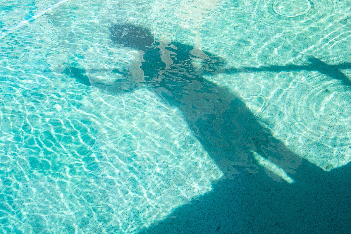 Shadow of a person underwater in a swimming pool with clear blue water reflecting the sunlight.