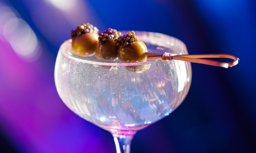 Cocktail in a long stemmed glass garnished with olives and caviar