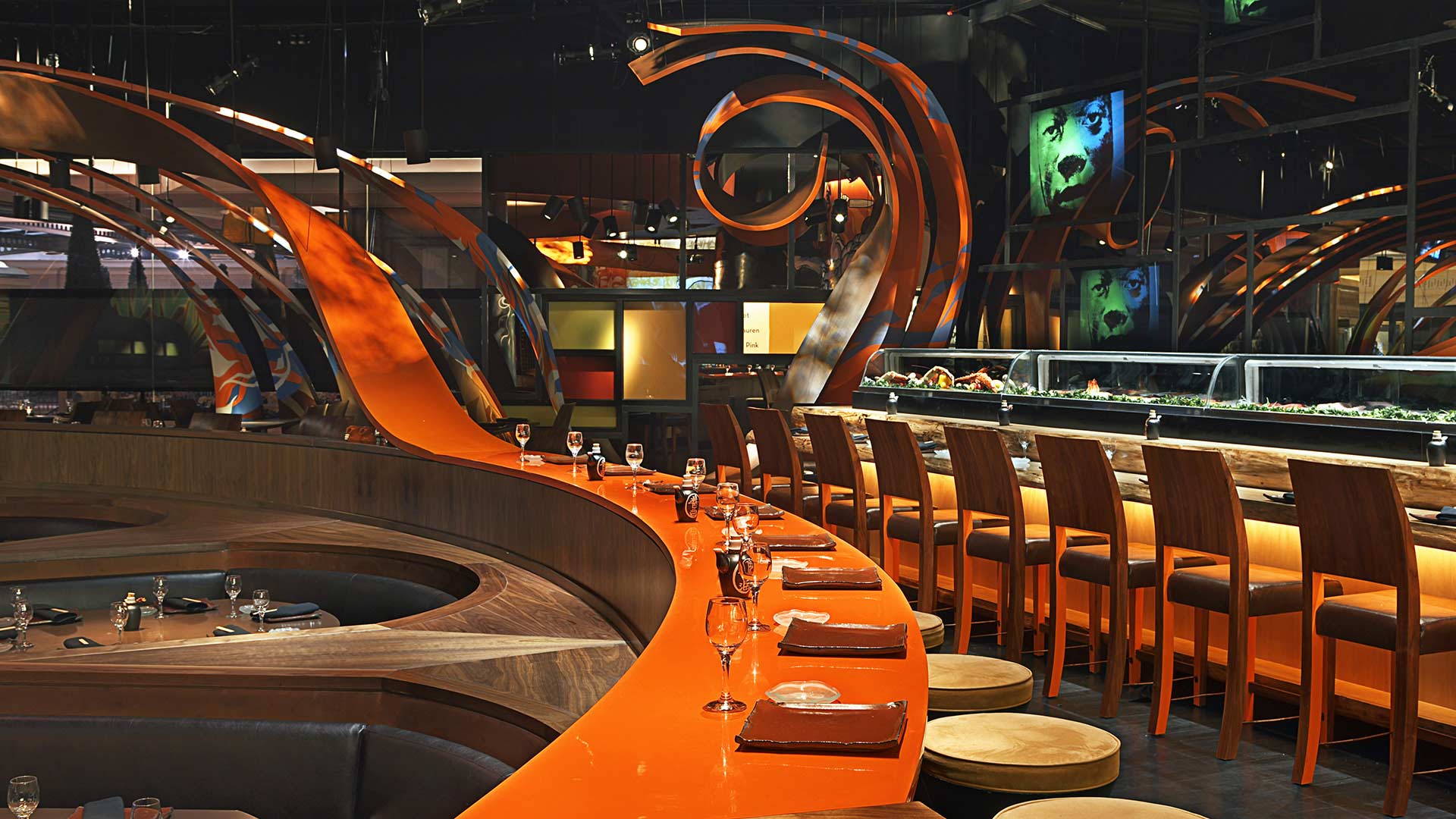 Modern restaurant interior with an orange sushi bar, high chairs, and artistic spiral designs on the walls and ceiling.