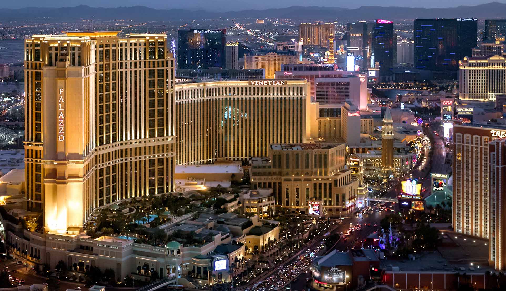 Aerial view of illuminated Las Vegas Strip at night, featuring the Palazzo and Venetian hotels and casinos.