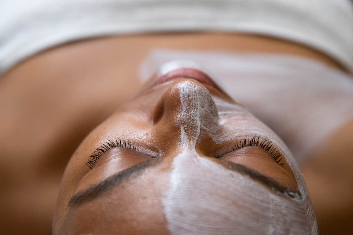 Person lying down with a white facial mask applied to their face, eyes closed, and wearing a white towel.