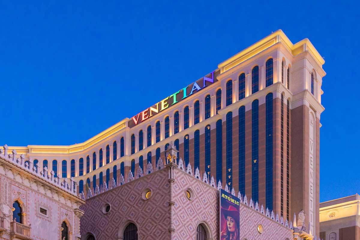 Exterior of The Venetian Resort in Las Vegas illuminated with colorful lights against a clear evening sky.