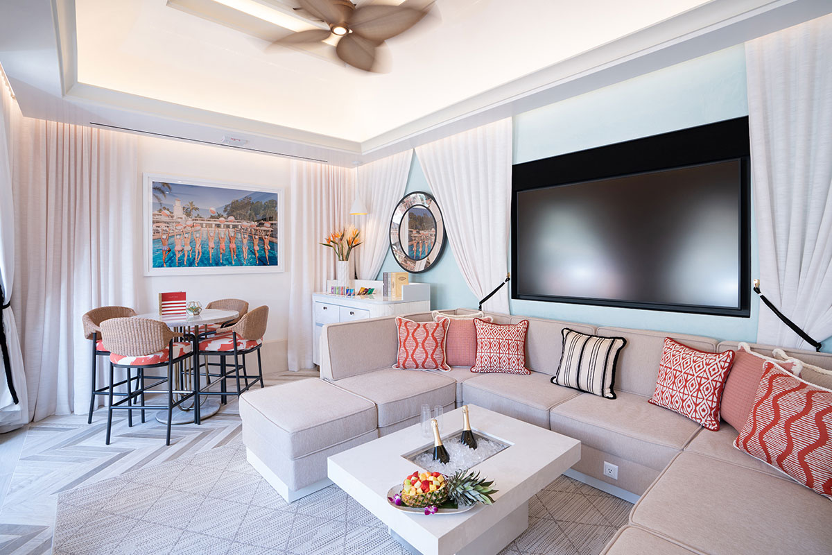 Modern living room with beige sectional sofa, red accent pillows, wall-mounted TV, round dining table, and framed artwork.