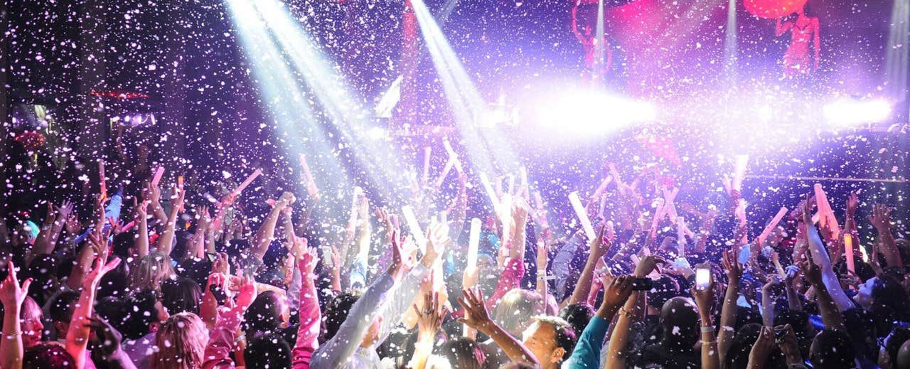 A large crowd enjoying a concert with vibrant lights and snow-like confetti falling from above.