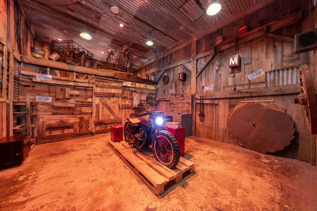 The garage in an abandoned wood cabin holding a motorcycle with its headlight on.