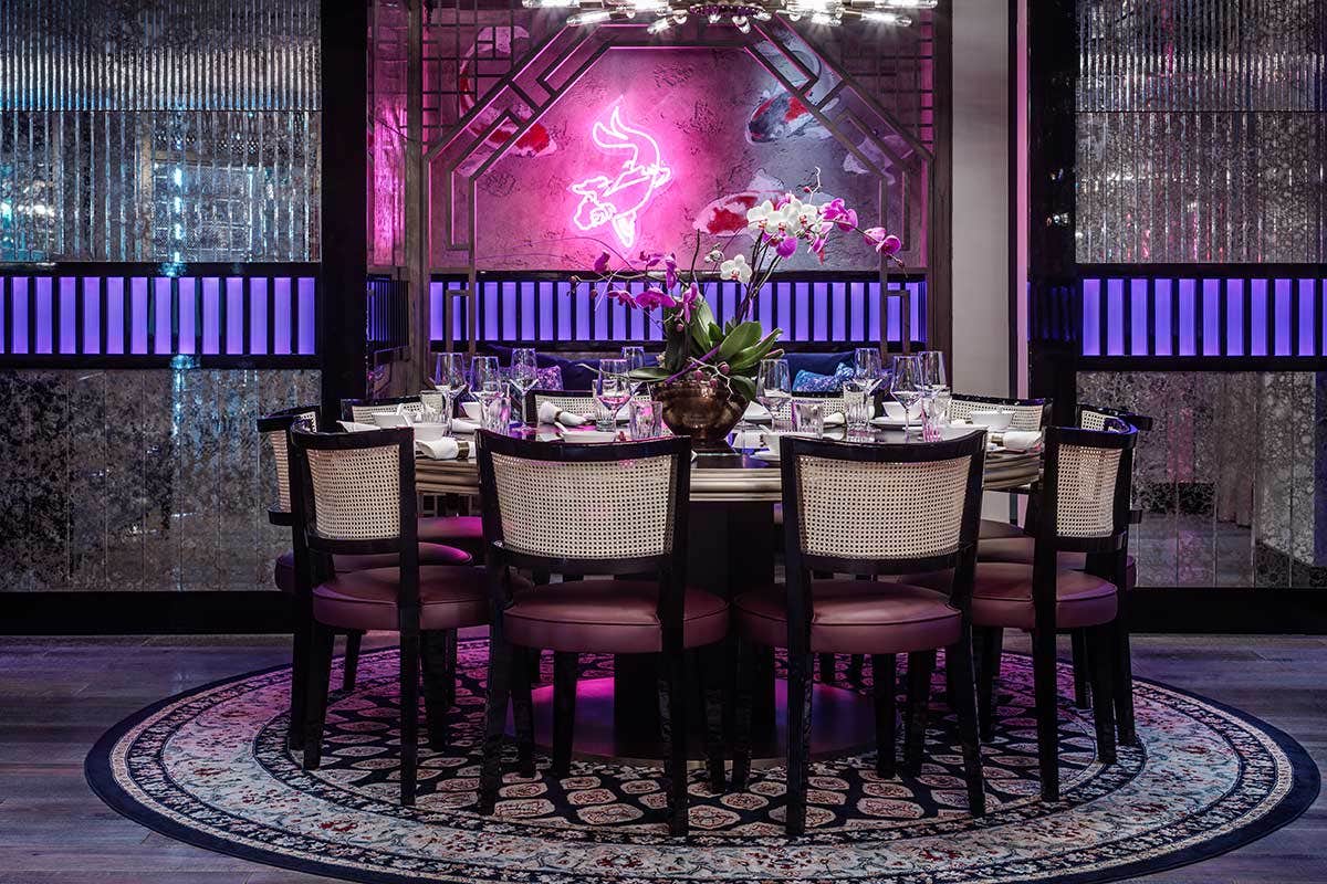 Elegant restaurant interior with neon pink lights, modern chandelier, and a round dining table set for eight.