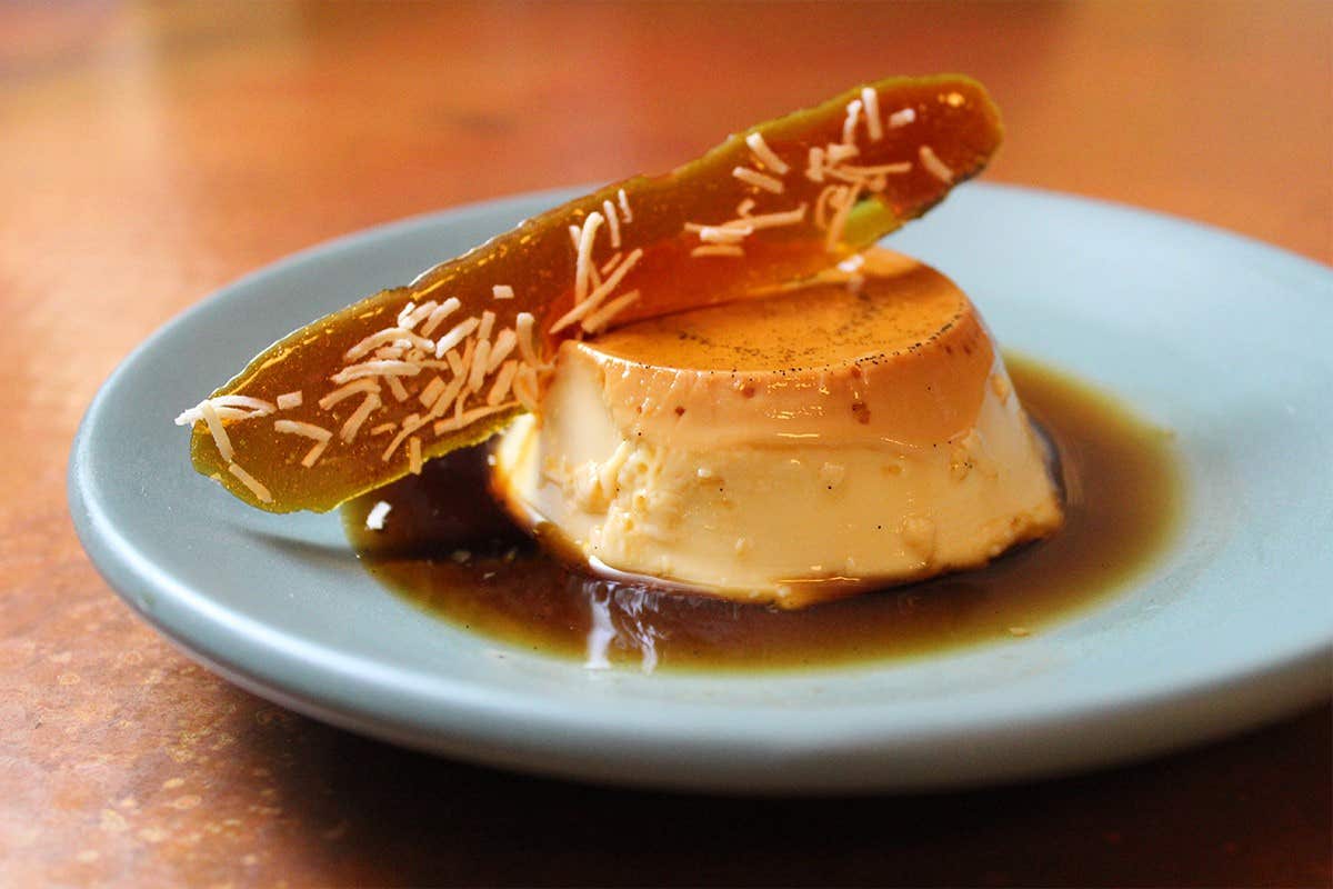 A plate with creamy flan topped with a caramelized sugar shard and garnished with shredded coconut.