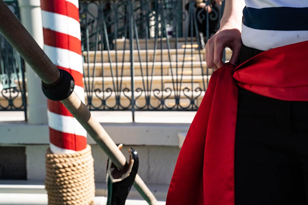 A person dressed in black pants and a white shirt with red sash stands near a large pole wrapped with red and white stripes.