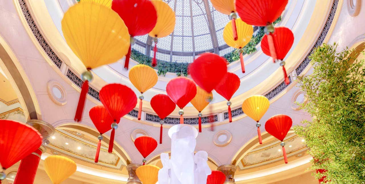 Red and yellow lanterns hanging from a ceiling with a glass dome, seen from a low-angle view inside an ornate building.