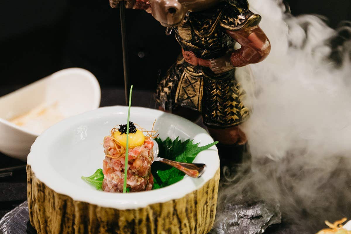 Plate with a gourmet dish garnished with caviar and egg yolk, served in a creative bowl with a statue and dry ice smoke.