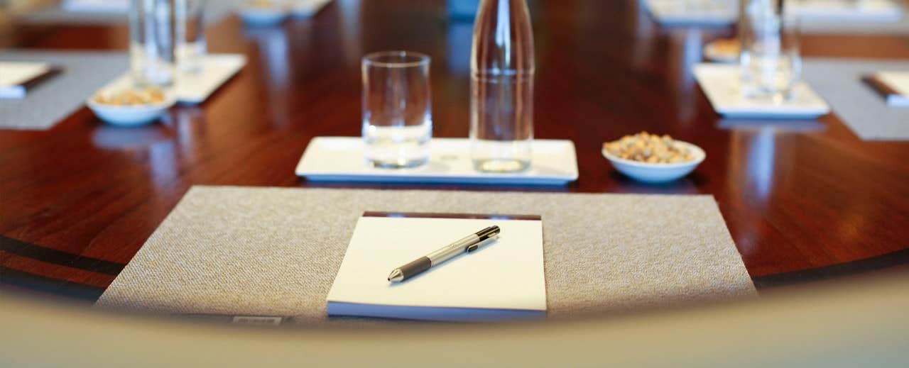 Close-up of a conference table with notepads, pens, water bottles, glasses, and bowls of snacks arranged neatly.