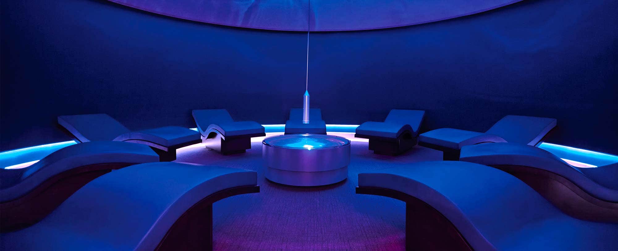 A dimly lit, circular room with lounge chairs arranged around a central glowing table.