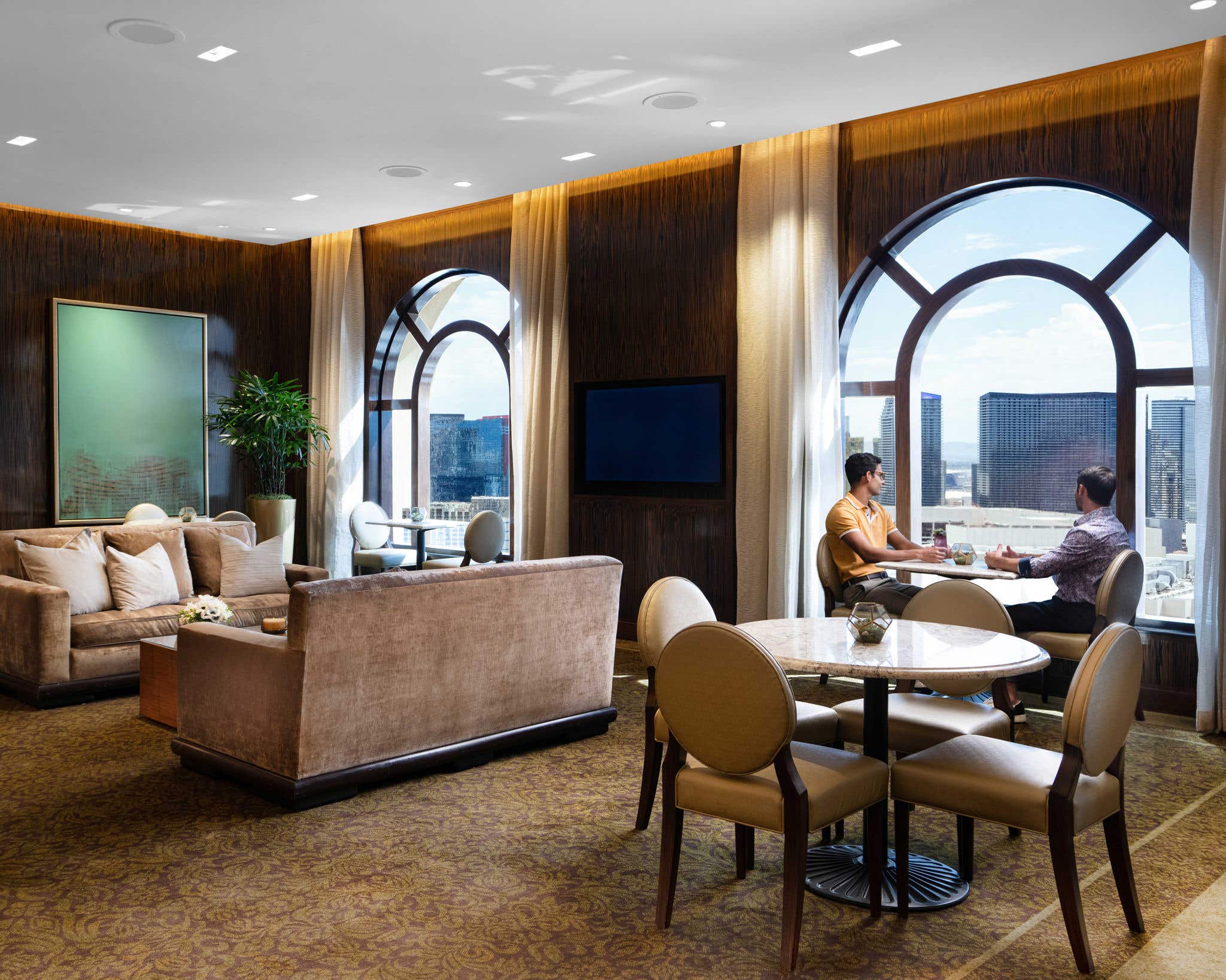 Two people seated next to an arched window in a Prestige Club Lounge overlooking the Strip.