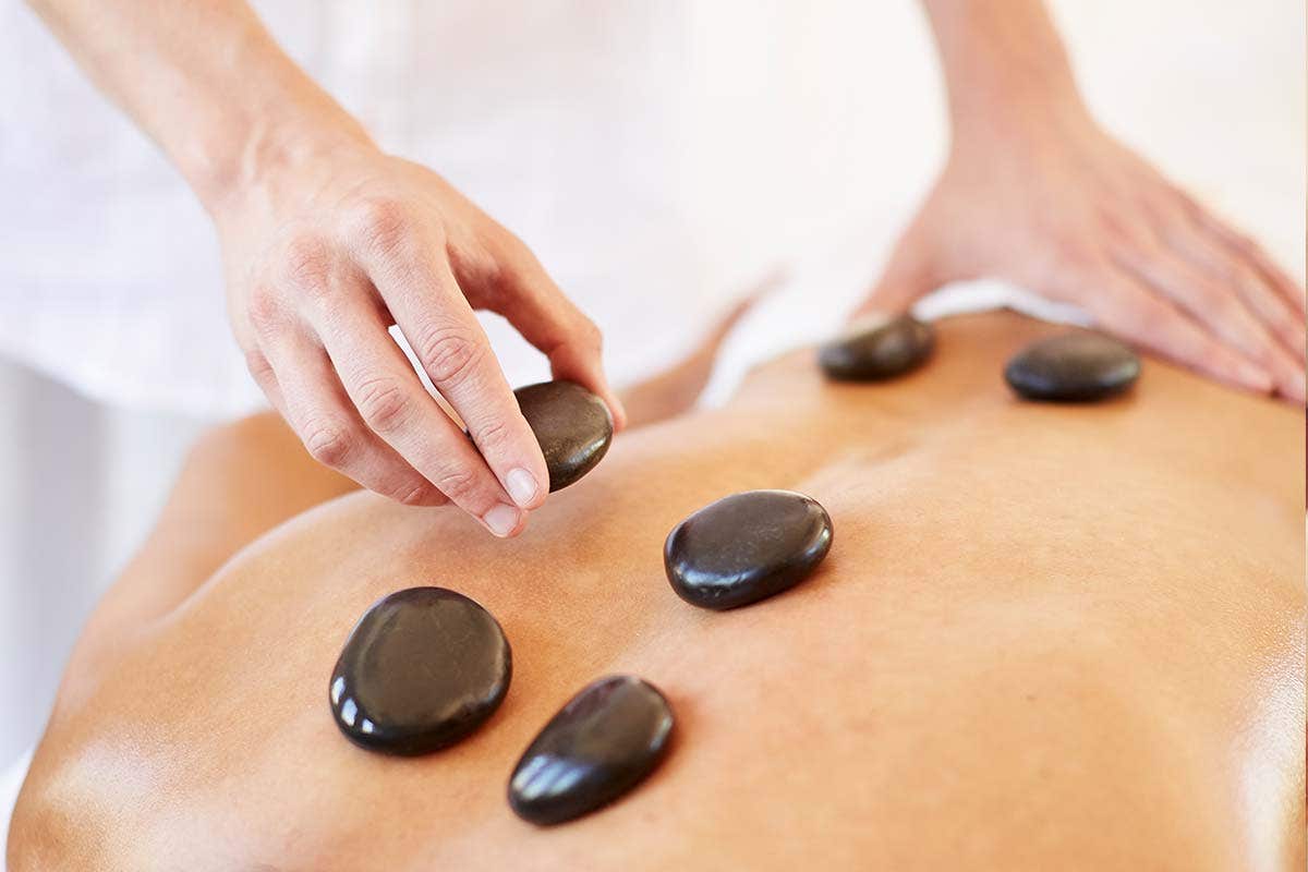 Person receiving hot stone therapy with smooth black stones placed on their back. Hands are arranging the stones.