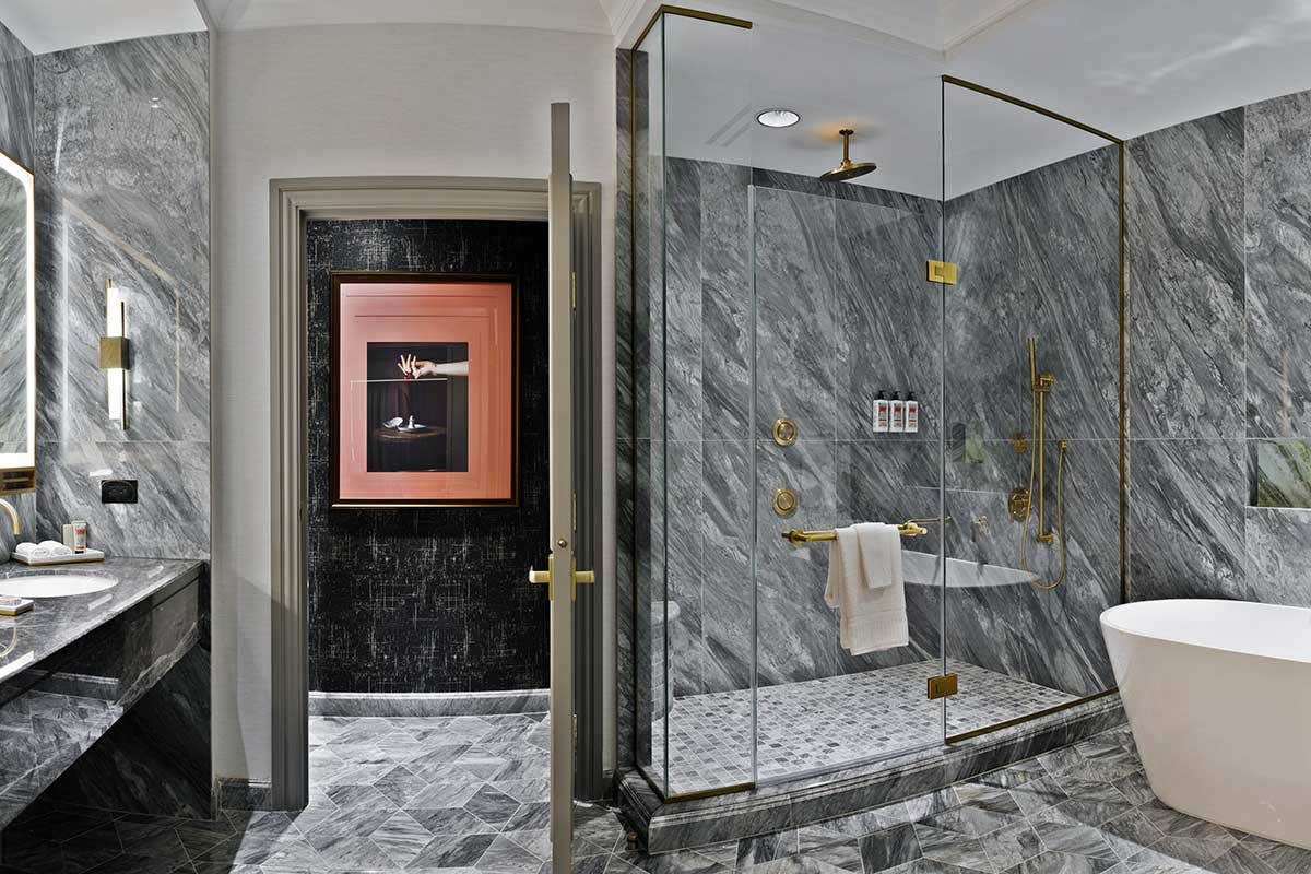 Luxurious grey marble bathroom with a glass shower, white bathtub, and dual sinks.