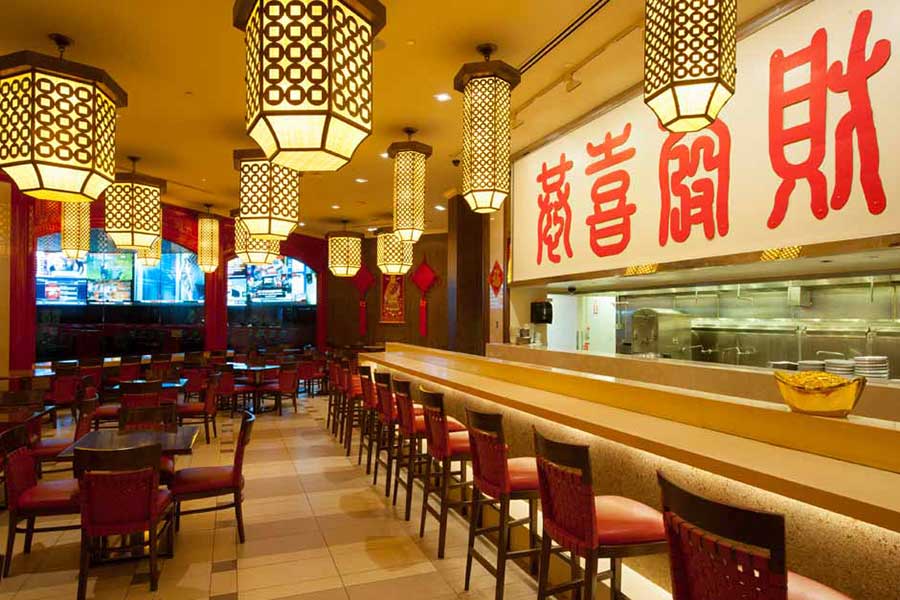 A brightly lit restaurant interior with patterned lanterns, a long bar counter, and a large sign with Chinese characters.