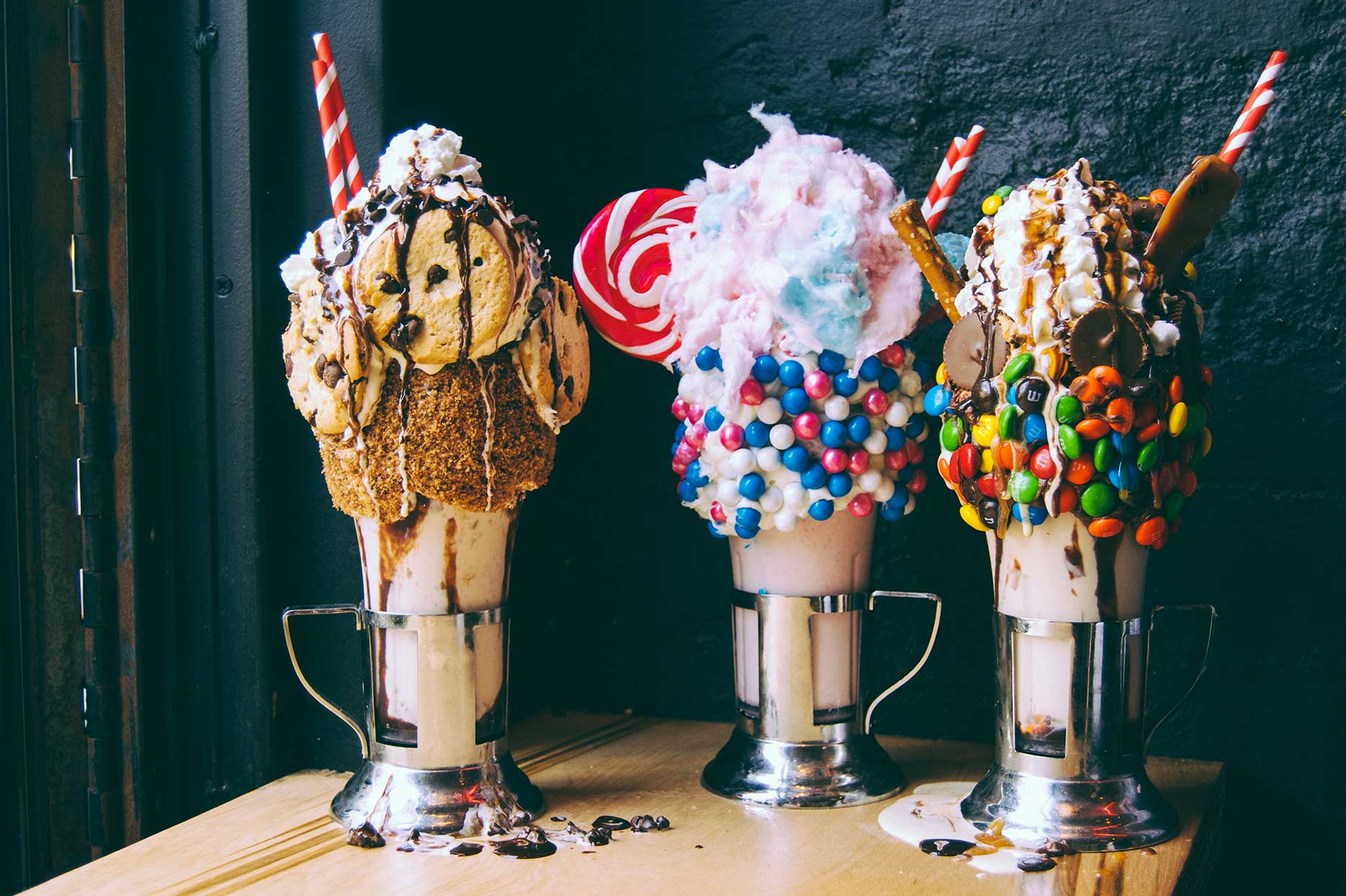 Three milkshakes heavily garnished with cookies, cotton candy and other candies.