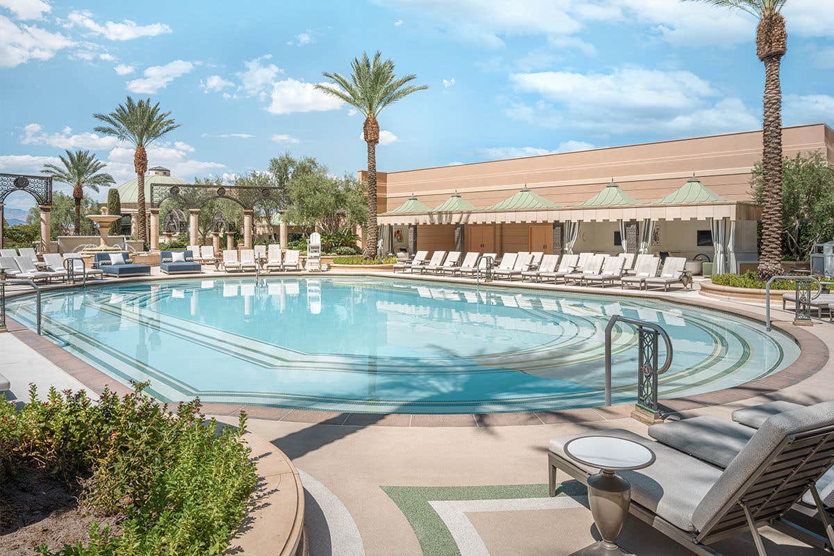 A pool on The Palazzo Pool Deck surrounded by pool chairs, palm trees, and cabanas in the background