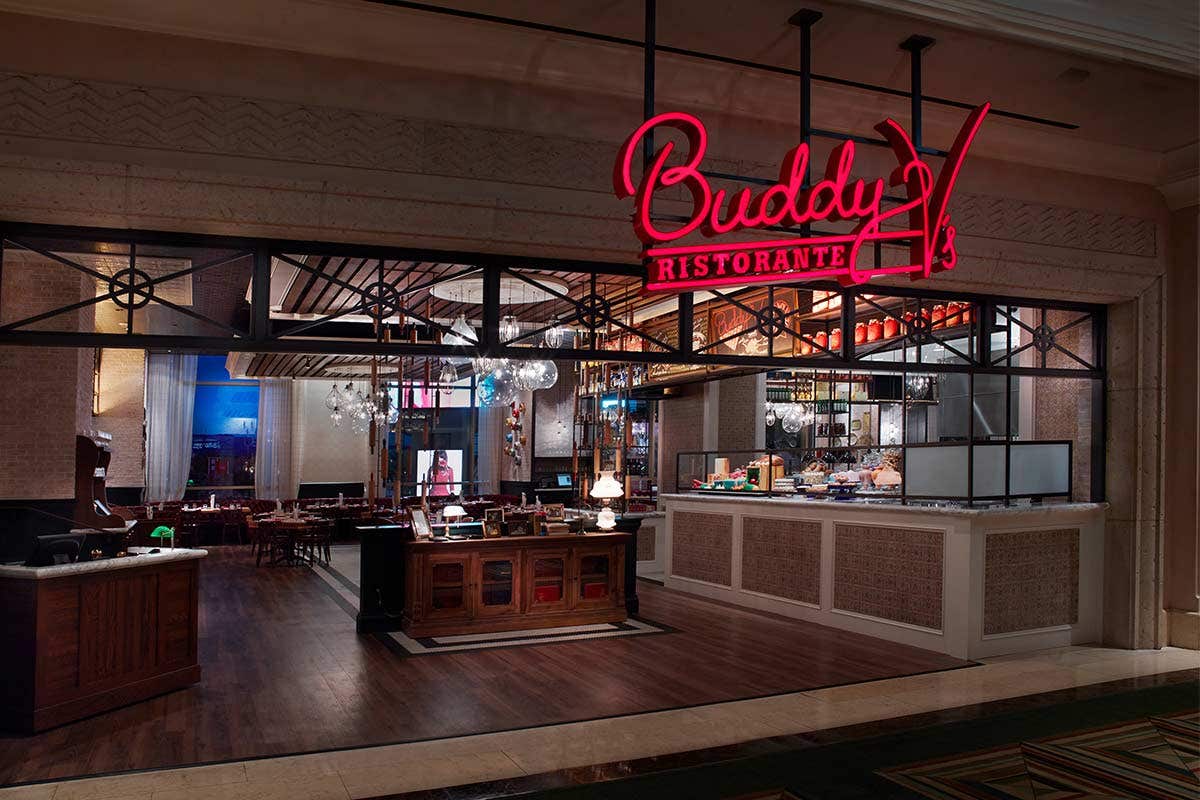 Exterior view of a restaurant named Buddy V's Ristorante with a stylish, warmly lit dining area visible inside.