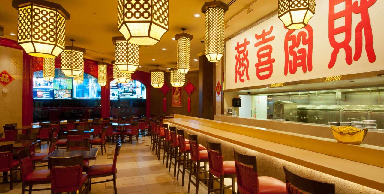 An empty Asian-themed restaurant with red accents, lantern-style lights, and a long counter overlooking an open kitchen.