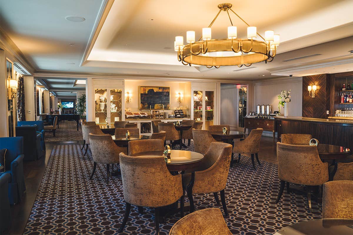 Elegant hotel lounge with cushioned chairs, round tables, a chandelier, and a buffet area with cozy ambient lighting.