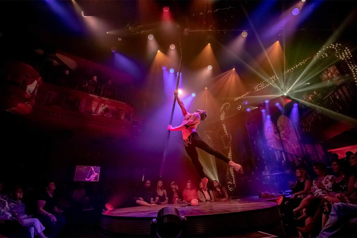 Aerial performer on a hoop in a dimly lit, vibrant stage with an audience watching.