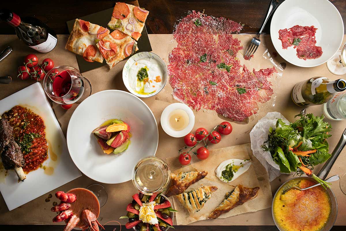 A table filled with a variety of colorful dishes including meats, salads, bread, tomatoes, and glasses of red and white wine.