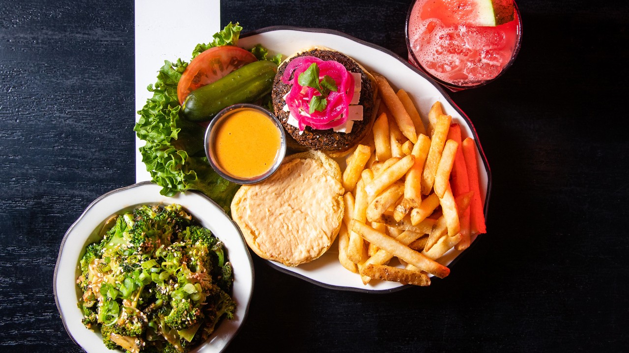 Plated meal with a burger, fries, salad, and a drink garnished with watermelon on a black and white background.