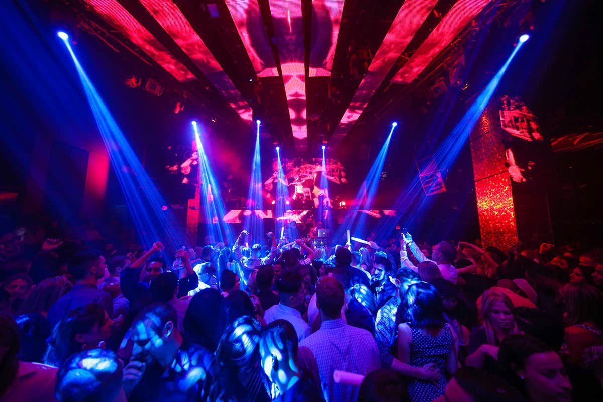 A crowded nightclub with colorful lights and beams illuminating people dancing.