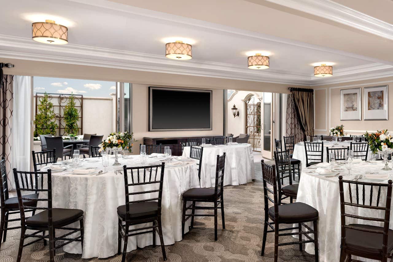 Elegantly set banquet hall with round tables, black chairs, and a large TV screen at the front. Flowers decorate each table.