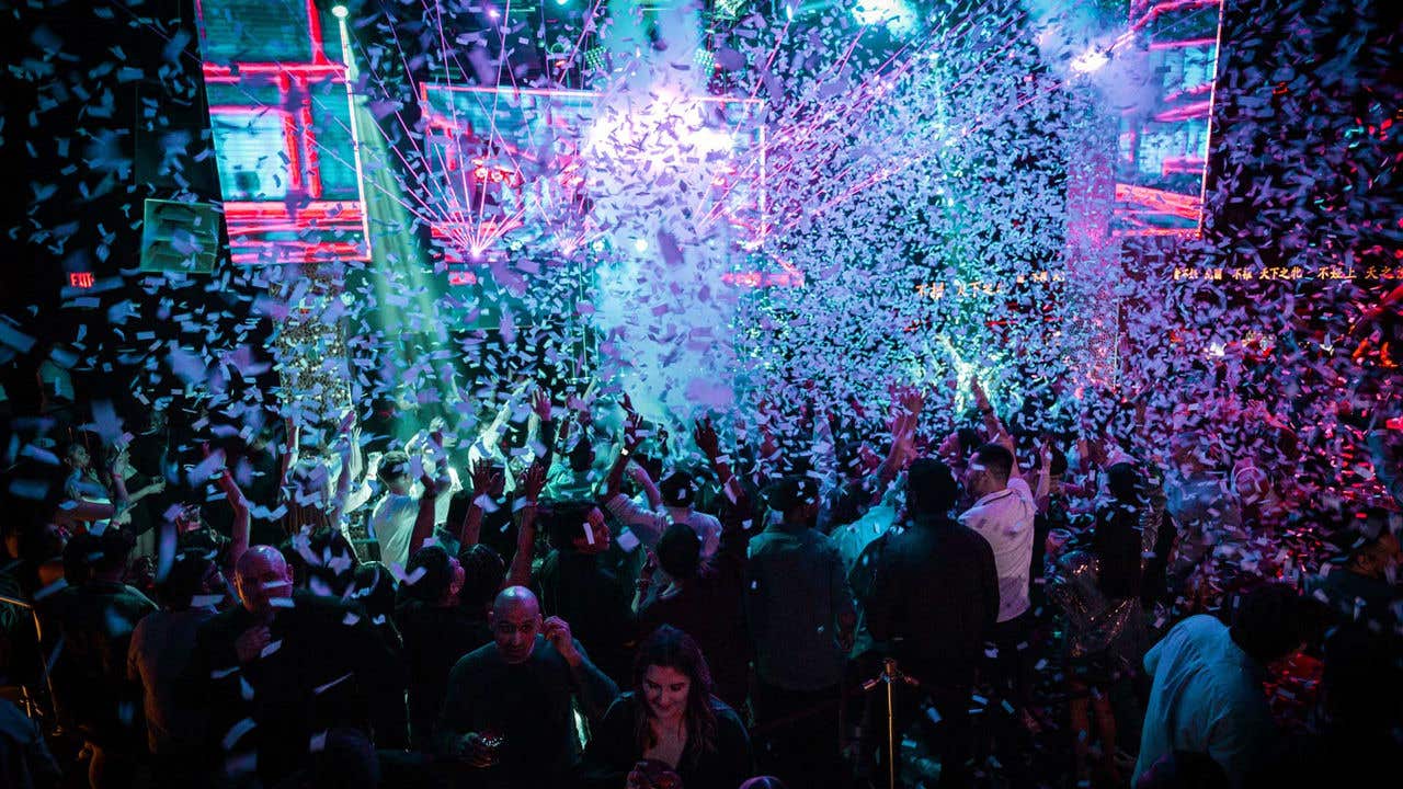 A crowded nightclub with colorful lights and beams illuminating people dancing.