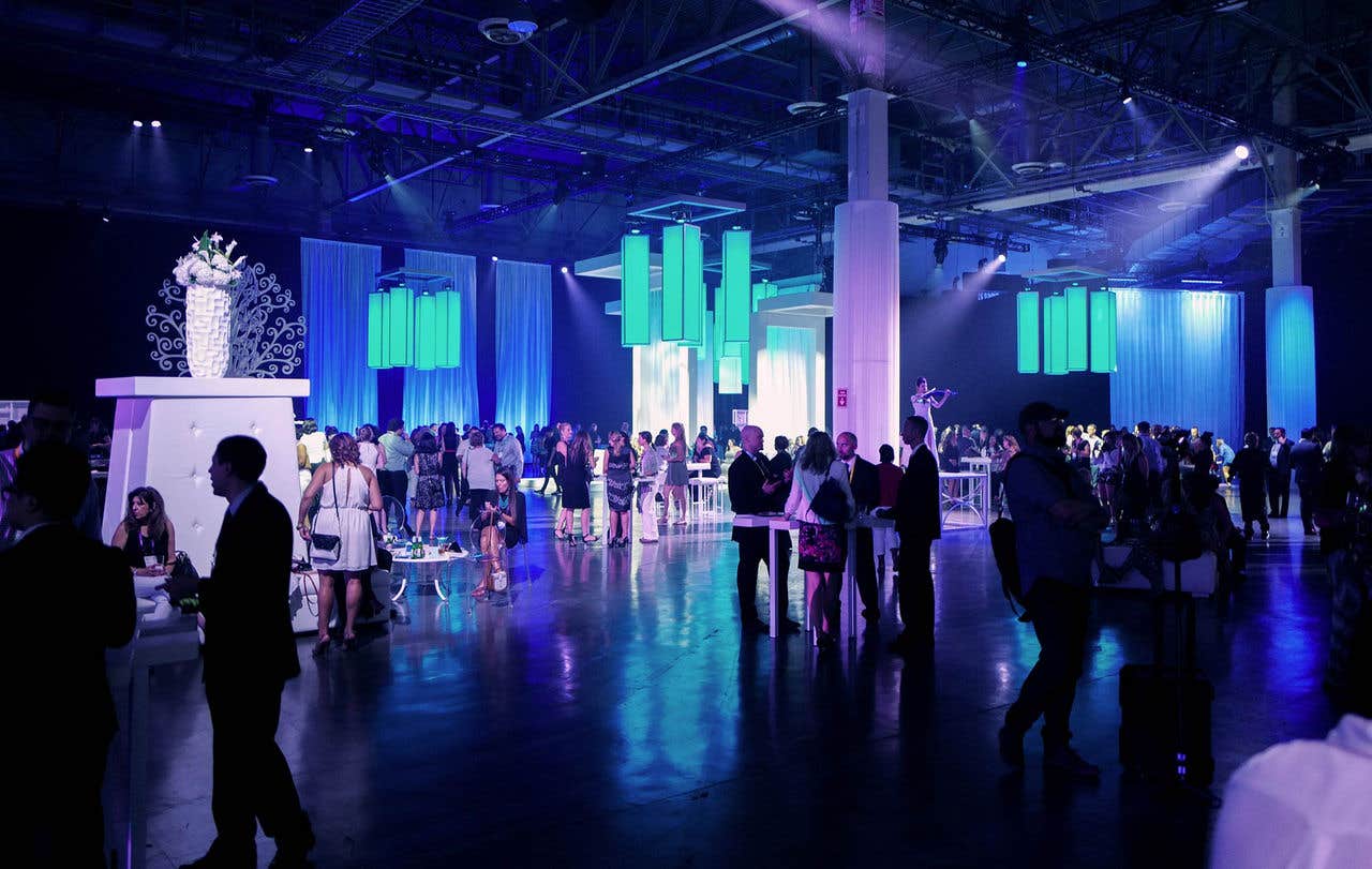 A dark lit expo hall with people mingling during an event. 