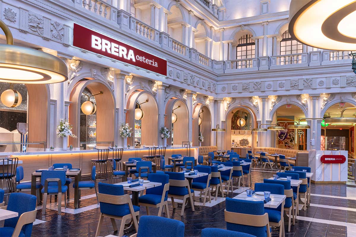 Modern restaurant with blue and wooden chairs, arched windows, and luminary fixtures. Sign reads "BRERA osteria.