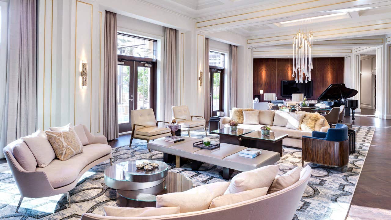 Luxurious living room with modern furniture, large windows, elegant chandelier, and grand piano in the background.