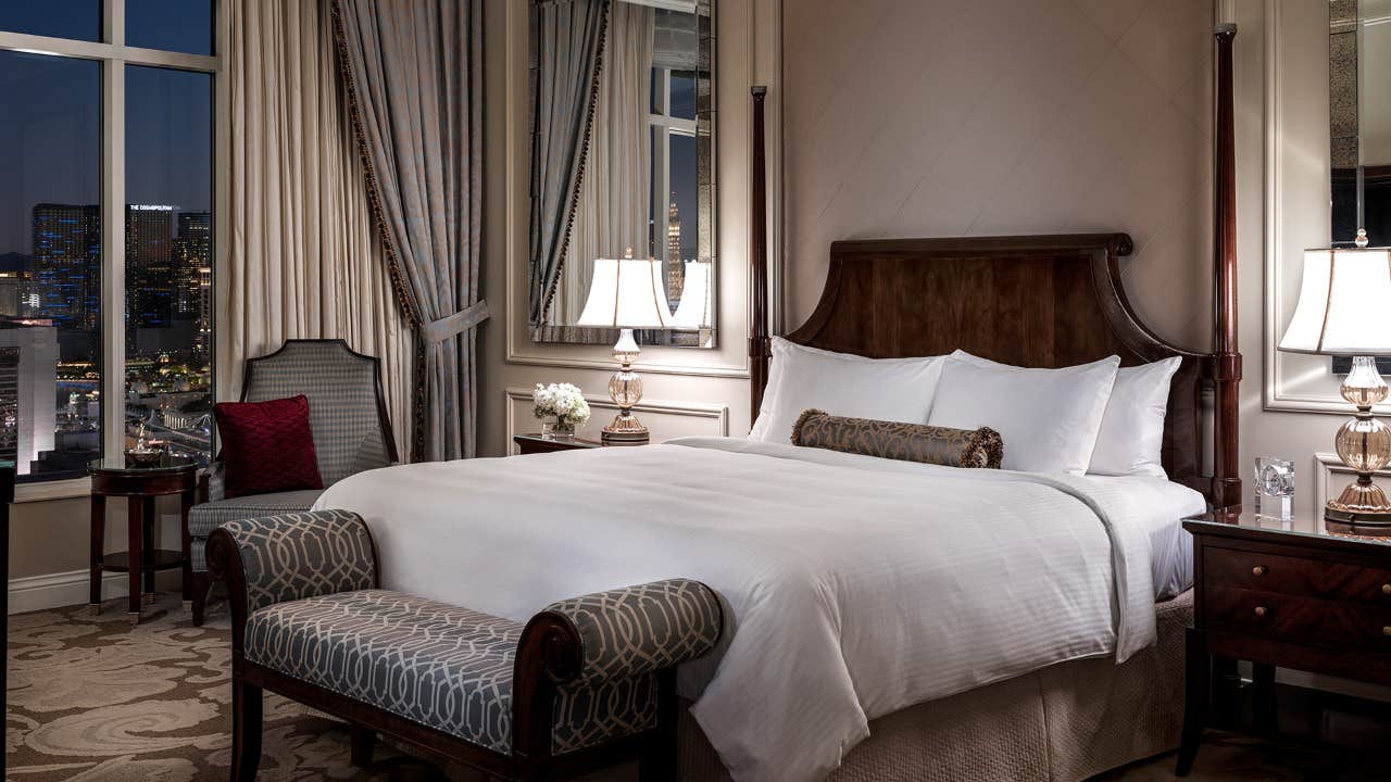 Luxurious hotel bedroom with a large bed, elegant decor, night city view through the window, and bedside lamps.