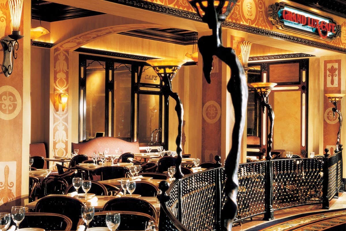 A warmly lit, elegant restaurant with ornate decor, neatly set tables, and intricate railings dividing the dining area.