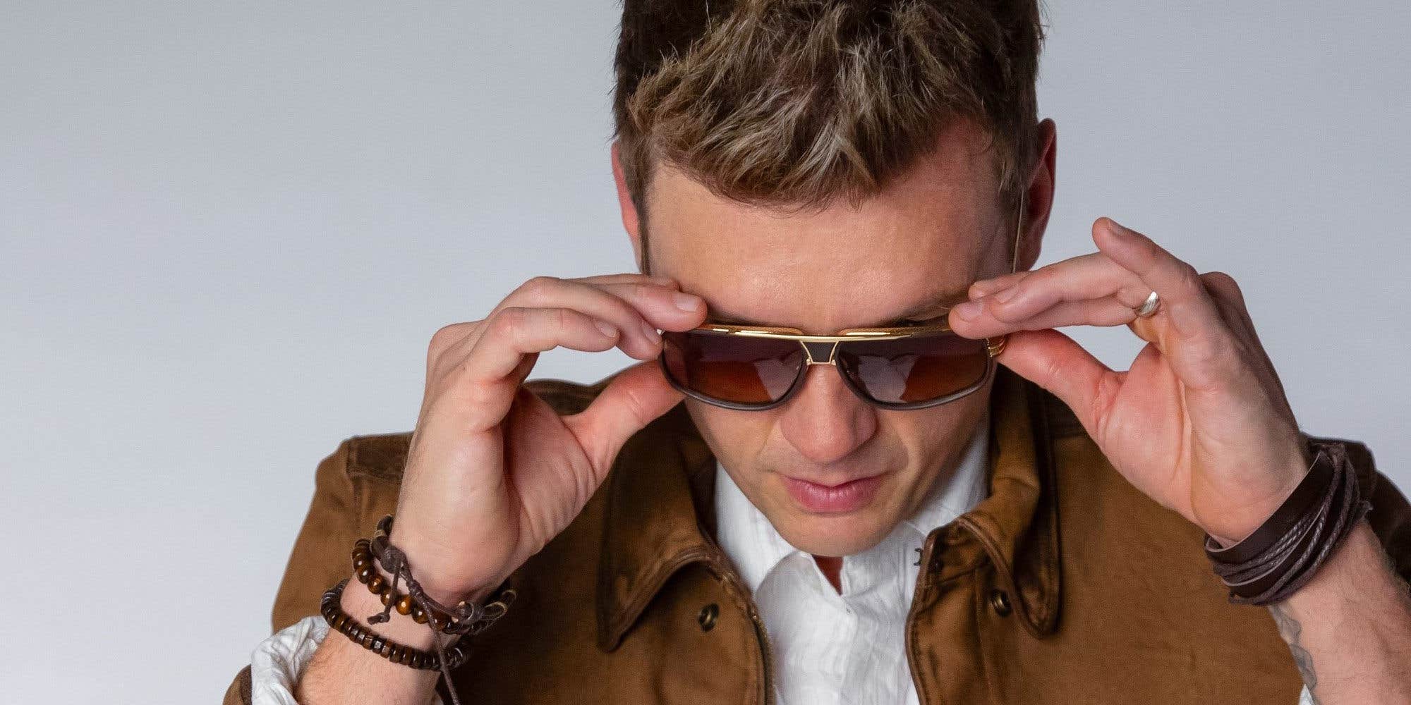 Nick Carter with his head tilted forward putting sunglasses on