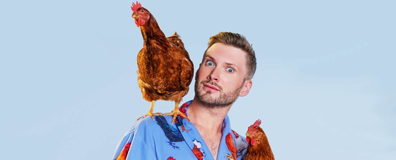 A man in a colorful shirt holds a chicken on his shoulder, with another chicken peeking over his shoulder.