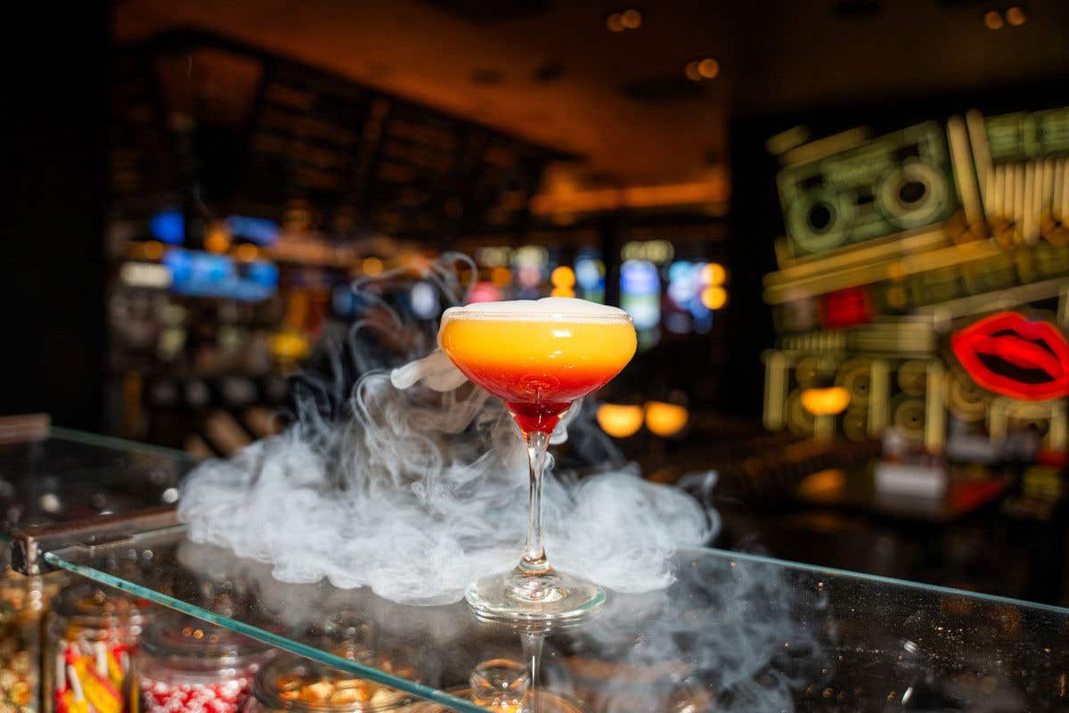 A colorful cocktail with smoke swirling around it in a bar setting.