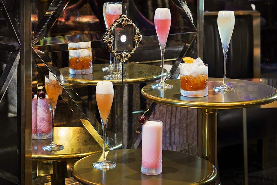 Assorted elegant cocktails in various glasses displayed on golden tables with a stylish, mirrored backdrop.