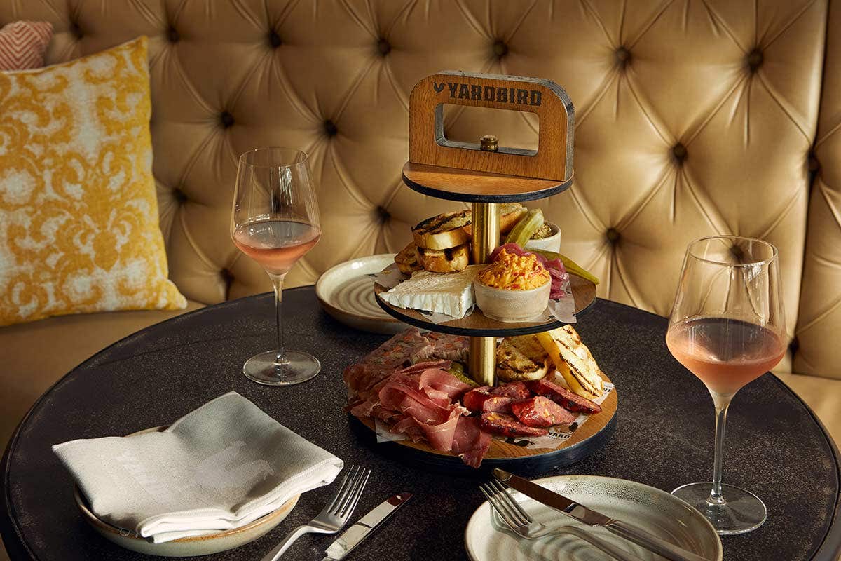 A round table with a two-tier charcuterie board, wine glasses, plates, and cutlery set for two at Yardbird restaurant.