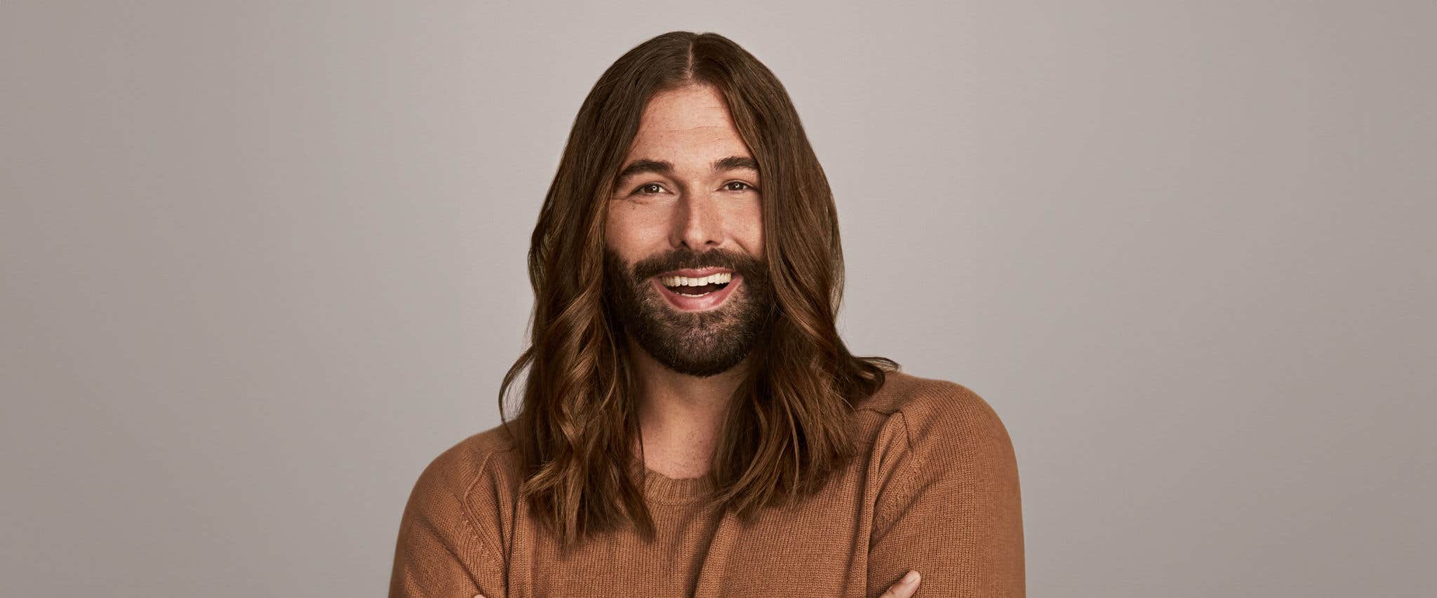 Jonathan Van Ness in a brown sweater in front of a gray backdrop