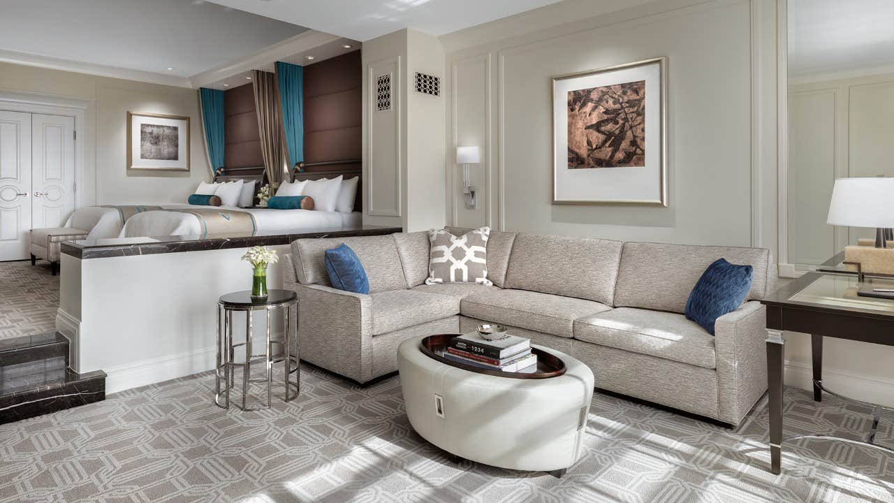 Luxurious hotel suite with a comfortable seating area, modern decor, and a spacious bed in the background.