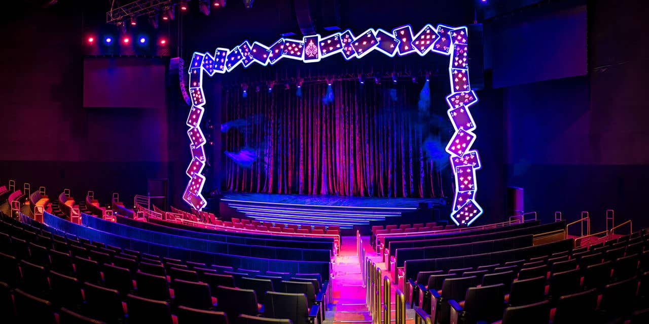 Palazzo Theatre stage framed with illuminated oversized playing cards, casting colorful beams onto the shimmering curtain.