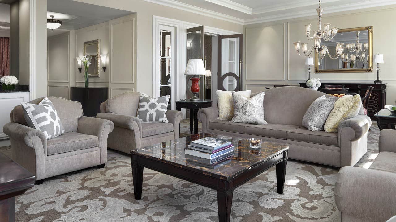 A stylish living room with a gray sofa, matching armchairs, a marble coffee table, modern decor, and a chandelier.