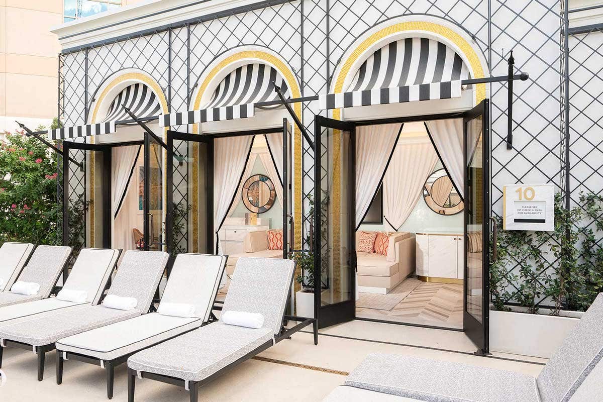 Poolside cabanas with striped awnings, cushioned lounge chairs, and elegant decor in a luxurious outdoor setting.