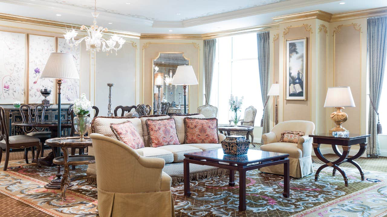 Elegant living room with classic furniture, ornate decor, large windows, and intricate patterned carpet.