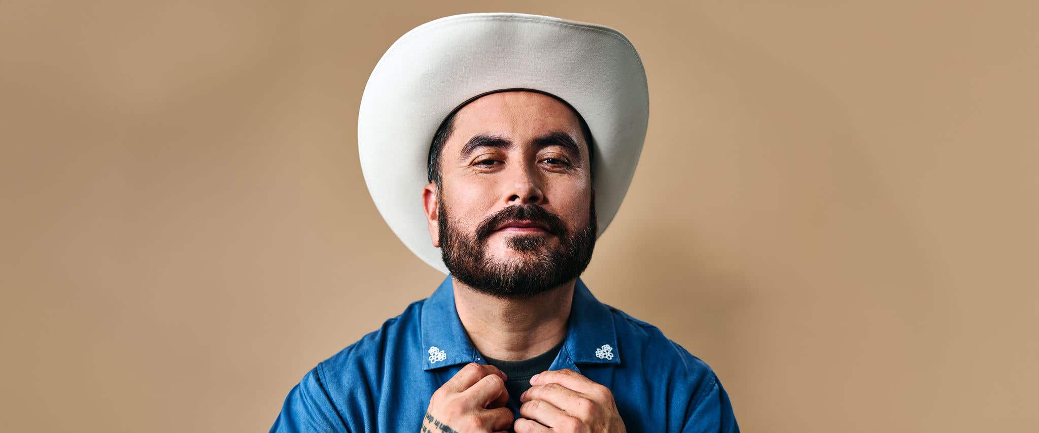 Alfred Robles wearing a cowboy hat and a blue shirt with white collar designs.